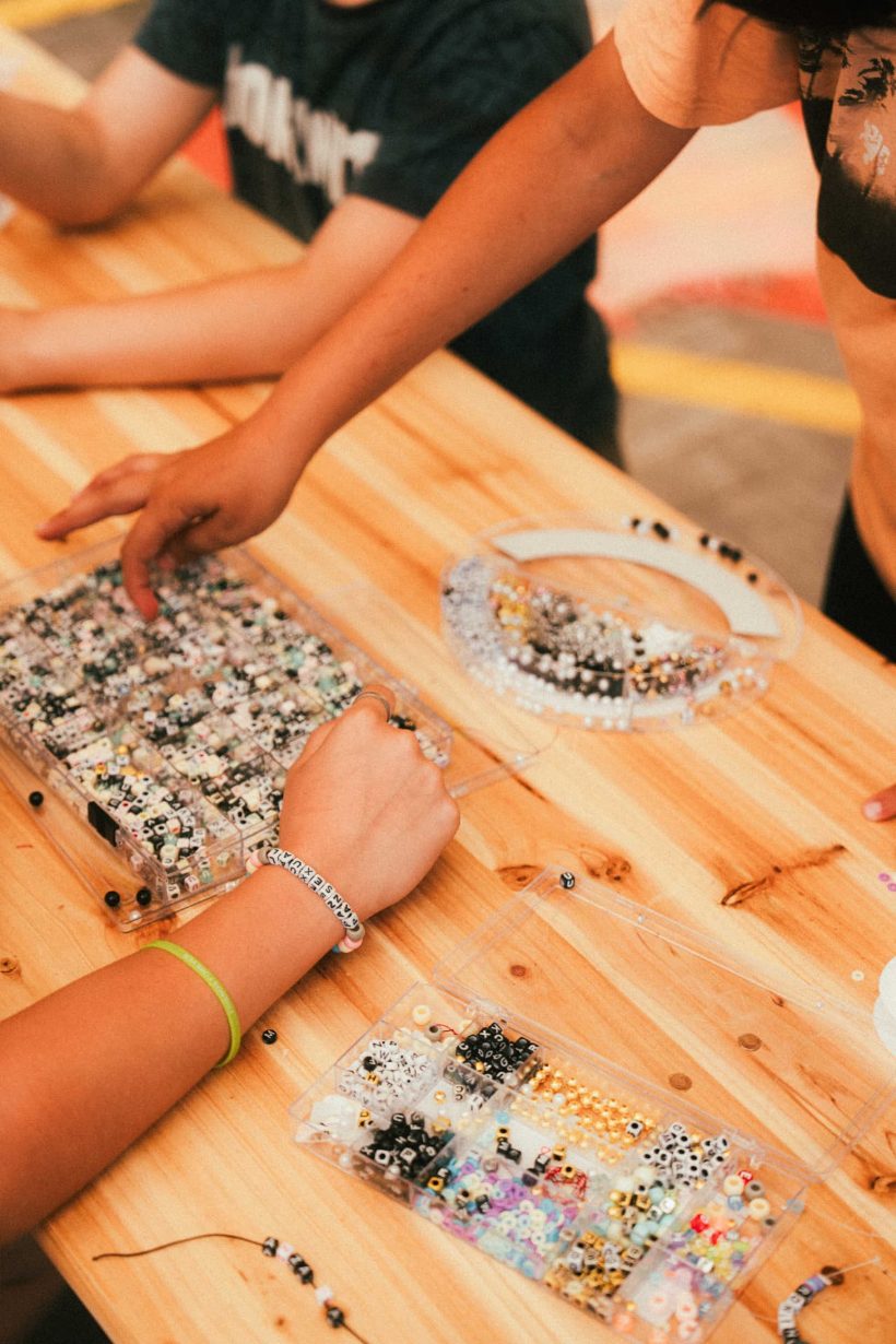 Jongeren maken samen armbandjes met kralen aan een houten tafel – talent & passion