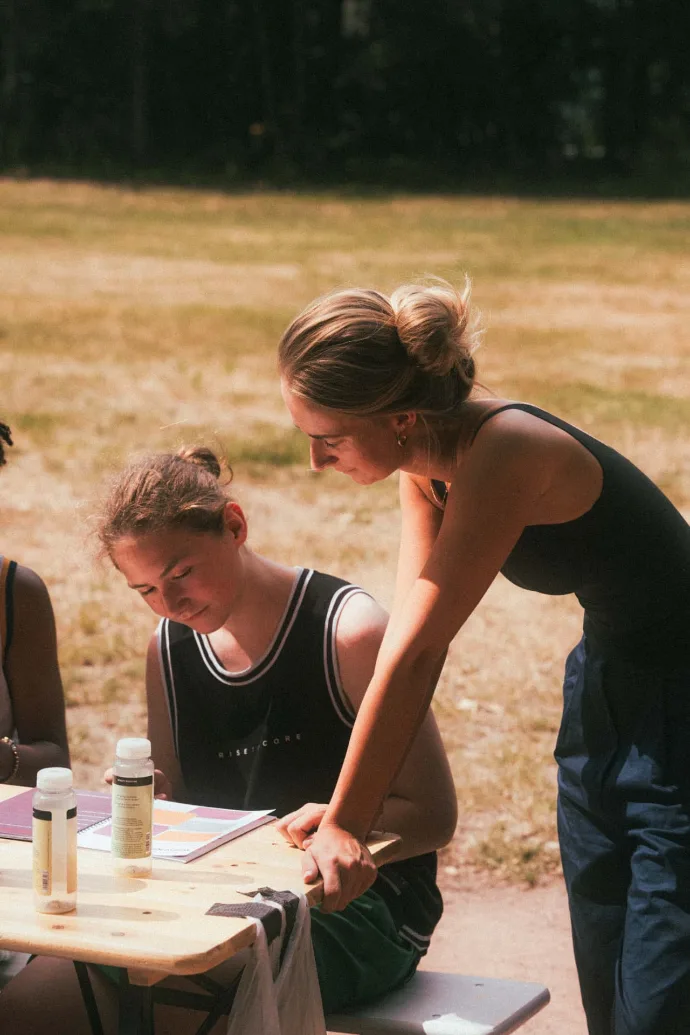 Coach helpt een deelnemer aan tafel tijdens een workshop op IMPACT [Camp]