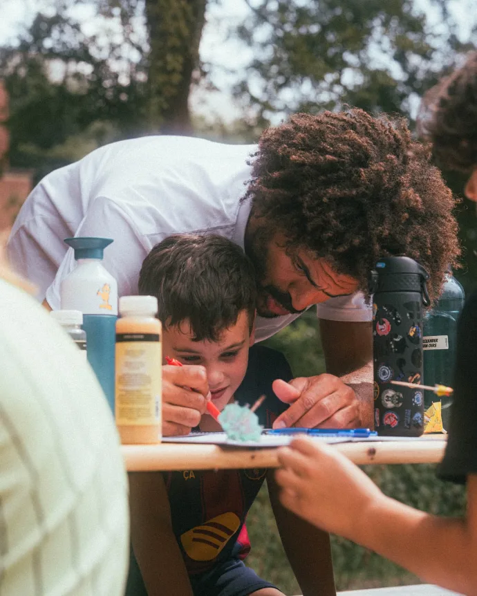 Coach en deelnemer buigen zich samen over een opdracht aan tafel tijdens IMPACT [Camp]